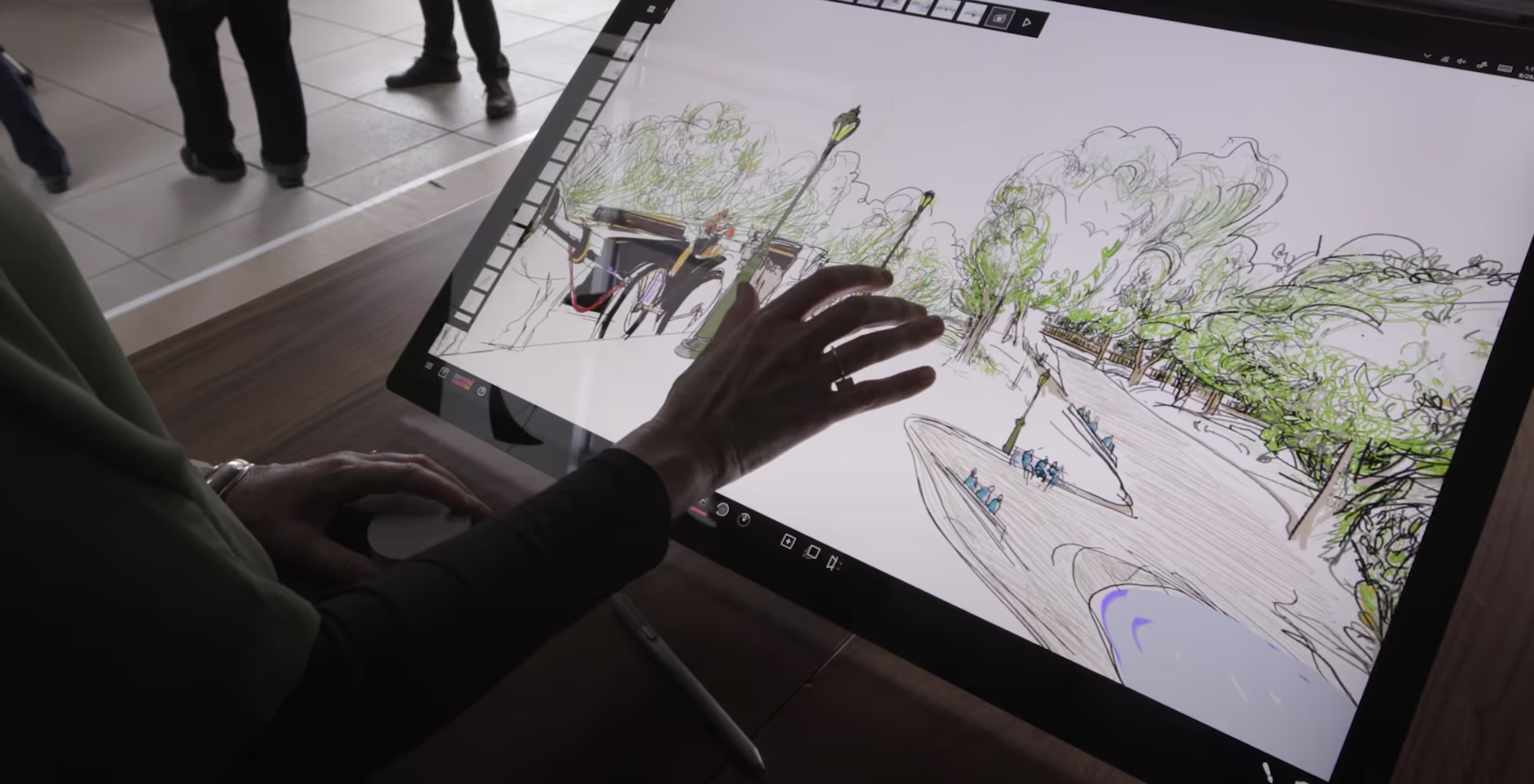 Shows a large Microsoft Surface tablet and an artists hand touching the screen.  The screen shows a Mental Canvas drawing of Central Park.